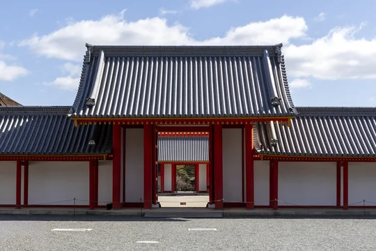 View of the traditional red gate and white walls of the Kyoto Imperial Palace under a blue sky in Kyoto, Kyoto, Japan.