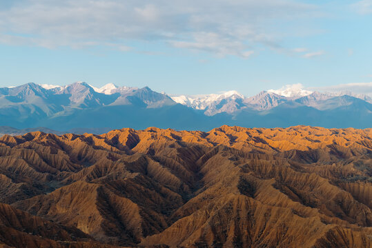 View of the eroded orange hills of Ak Say Canyon and the Valley of Forgotten Rivers with snow-capped mountains in the distance Ak Say, Issyk-Kul Region, Kyrgyzstan.