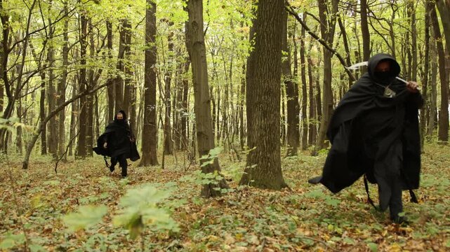 enemy's attack, forest path, occult forest. Two hooded individuals dressed in dark robes walk through thick autumn woodland, creating mood filled with fantasy or horror and intense suspense.