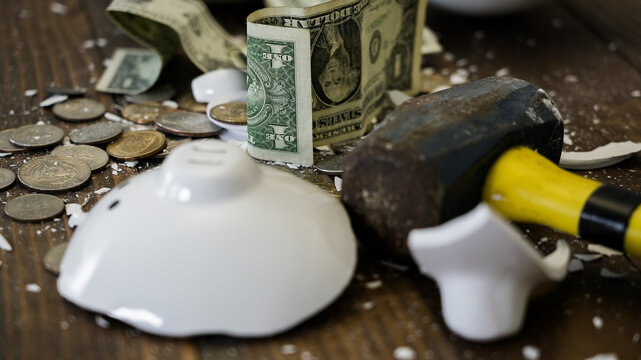 Broken piggy bank with money and hammer showing financial crisis