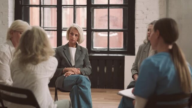 Sad blonde woman listening to colleagues on business meeting or participant of group therapy in psychological clinic. Vertical portrait of mature lady thinking about life problems and relationship