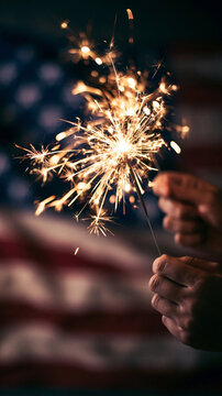  Hands holding a burning sparkler against a blurred American flag background. Patriotic 4th of July Independence day celebration concept