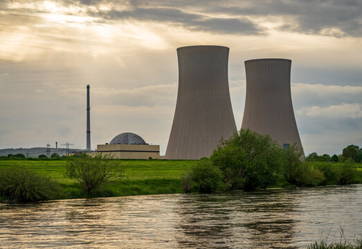 The Grohnde Nuclear Power Plant features impressive cooling towers and reactor dome in Lower Saxony, Germany with the River Weser in the foreground