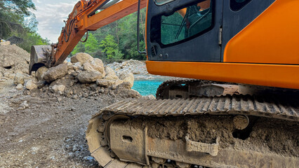 Orange excavator on rocky riverbank in soft daylight by turquoise water ideal for construction editorial environmental reports and social media, 5 May 2026 Subitica, Serbia © fotoworld