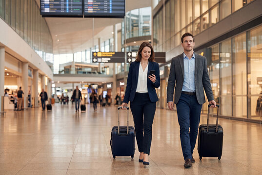 Business travelers walking with luggage through modern airport terminal