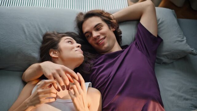 Joyful lovers resting pillows home top view. Girlfriend boyfriend touching hands