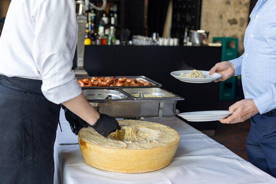Cooking pasta in cheese wheel at a restaurant during a food event in the evening with guests enjoying the meal