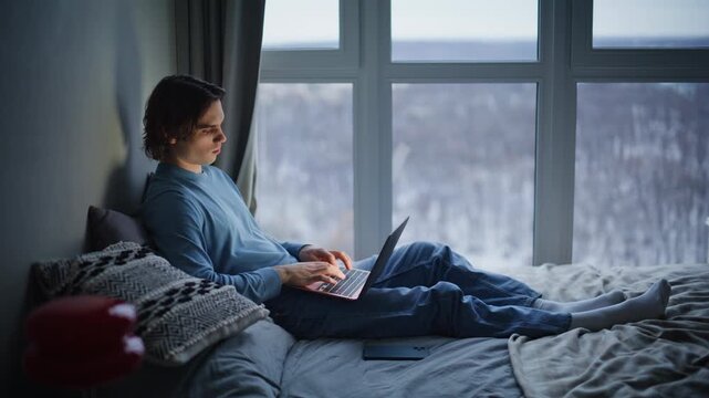 Evening guy thinking laptop in bed enjoying calm weekend home. Thoughtful author