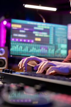 Sound engineer working with soundboard and midi controller to create the perfect tunes for his songs, recording and editing audio. Music composer adjusts volume levels during mixing sessions.