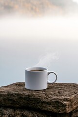 Obraz premium Steaming cup of coffee on a stone surface near water during early morning