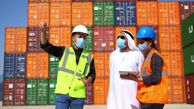 Arab businessman in kandura and logistics workers in masks discussing cargo details with digital tablet in front of colorful shipping containers stock video.