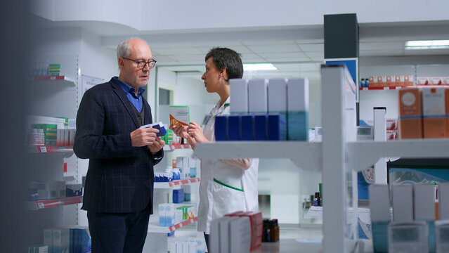 Older man feeling unwell visiting pharmacy, looking to find pharmaceutical product to cure nauseating affliction, asking licensed healthcare employee for product suggestions.