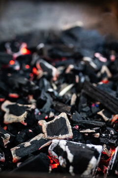 Glowing charcoal embers and black burned wood pieces for outdoor barbecue cooking.