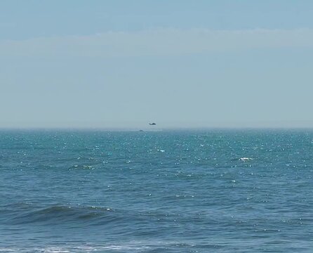 Low hovering Coast Guard rescue helicopter over a disabled boat in the ocean
