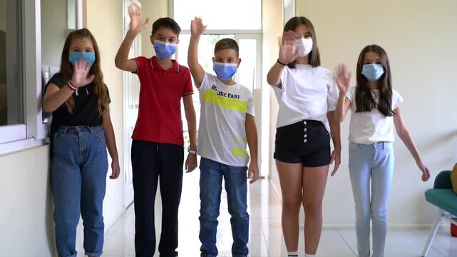 Group of school children in masks waving hands then taking off face masks in school corridor, back to normal education concept stock video.