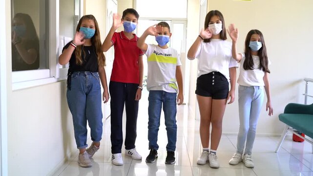 Group of school children in masks waving hands then taking off face masks in school corridor, back to normal education concept stock video.
