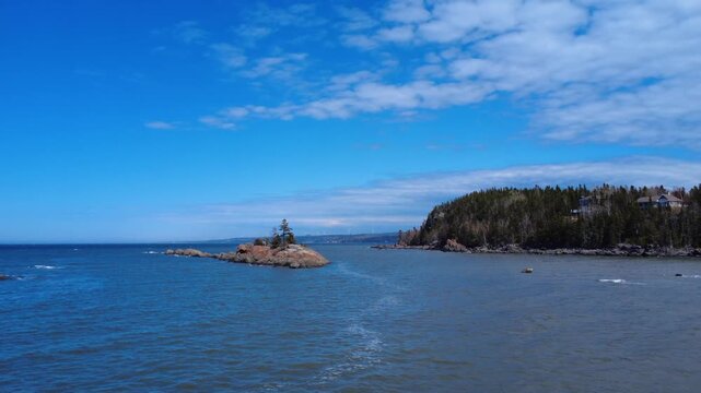 Drone footage of &Icirc;le-aux-Trois-Sapins, a rocky islet with resilient fir trees, surrounded by the scenic waters of the St. Lawrence River in Quebec, Canada.