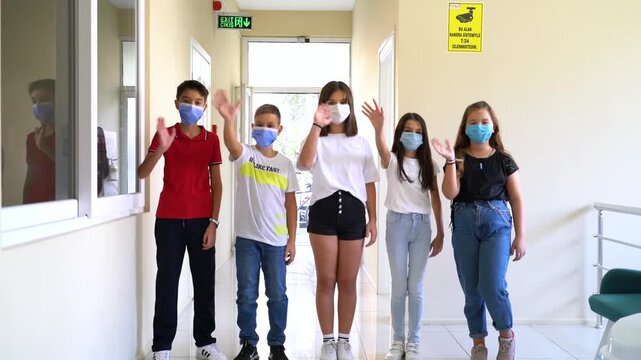 Group of school children in masks waving hands then taking off face masks in school corridor, back to normal education concept stock video.