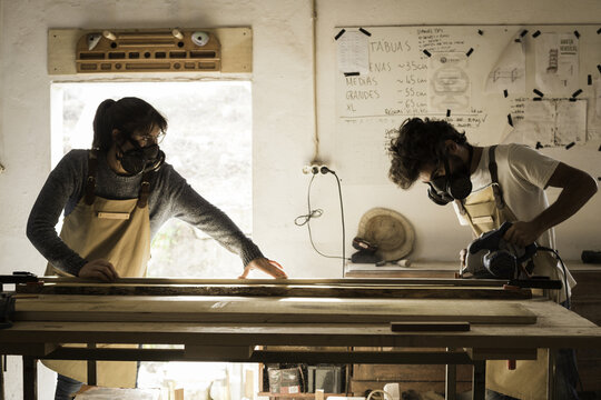 View of two woodworkers wearing protective masks and aprons cutting a wooden plank in a workshop in Lisbon, Lisbon, Portugal.