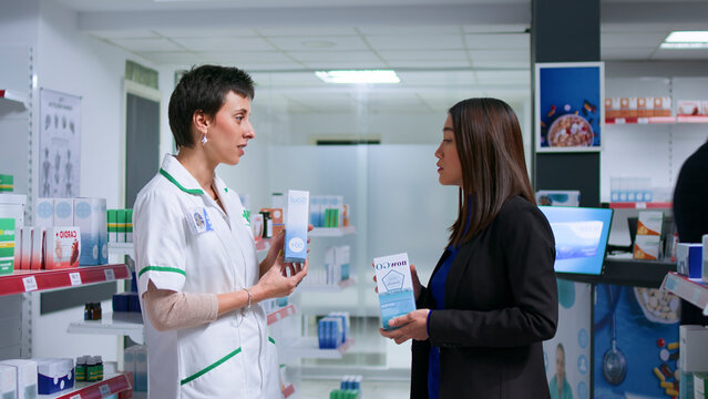 Asian customer feeling unwell visiting chemist shop, looking to find pharmaceutical product to cure nauseating headache, asking qualified healthcare expert.