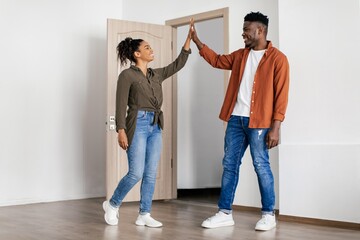 Fototapeta premium Joyful Black Couple Celebrating New Home By Giving High Five In Modern Apartment Interior, Smiling And Enjoying Togetherness In Bright Room. Home Lifestyle Concept.