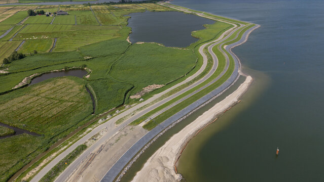 Aerial view of the dike reinforcement project along the coastline with a winding road, green embankments, and sandy construction works in Uitdam, North Holland, Netherlands.