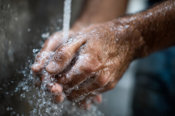 Fototapeta premium Water cascades over rough, weathered hands. Fingers twist under steady, cold stream. Skin shows age, dirt, and daily labor. Close-up captures clean, personal hygiene act. Ideal for health, wellness