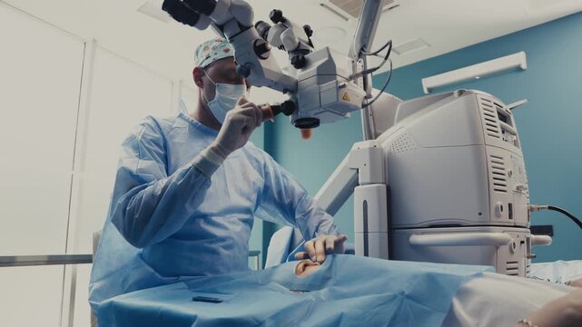 Male surgeon in blue surgical attire performs eye surgery using a microscope in a modern medical facility with bright lighting and clean surroundings