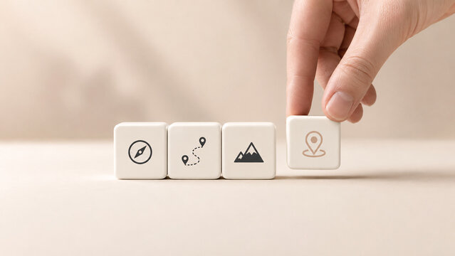 Hand arranging wooden cubes with travel planning icons including compass route map mountain and pin pointer location on beige background concept for trip itinerary navigation and tourism search