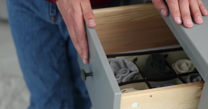 Man putting socks into drawer with organizer at home, closeup