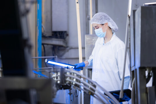 Female quality control workers using UV light to inspect production line in food factory, Technician team in white lab coats performing hygiene audit on industrial canning line in manufacturing plant