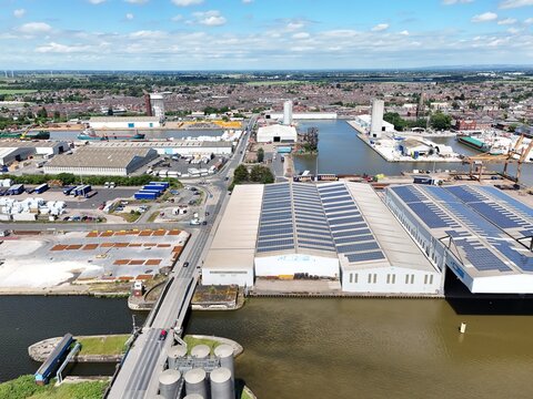 Aerial view of the industrial port area featuring large warehouses with solar panels, a canal, and a bridge, set against the urban landscape of Goole, England, United Kingdom.
