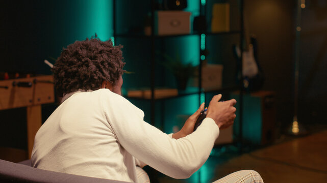 Man in rgb lit apartment using cloud gaming service to play demanding competitive multiplayer SF video game on TV, player streaming game online, using motion controlled controller gadget to play.