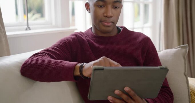 African American male 20s in maroon sweater holding tablet in folio on couch reacting to content
