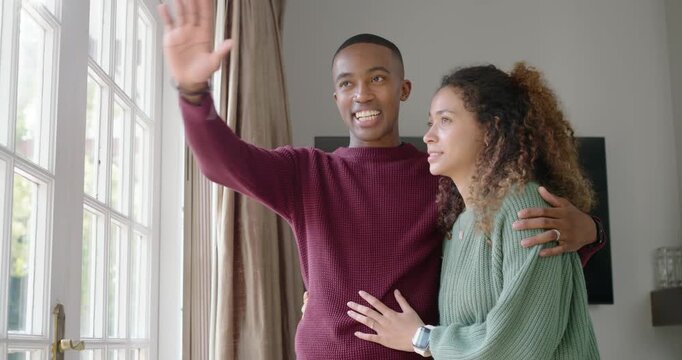 Diverse couple in sweaters at paned door, man spotting view, wrapping and pointing, woman listening
