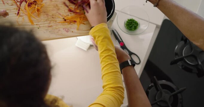 After peeling strips, diverse couple in kitchen, woman in yellow tipping board into cooker for meal