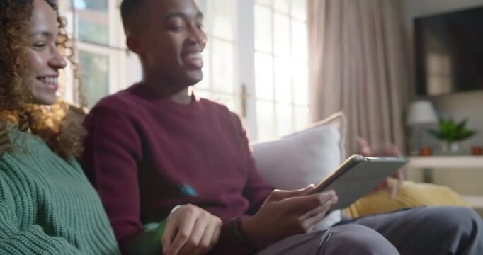 Couple woman pointing tablet, African American man turning and scrolling, sharing content on couch