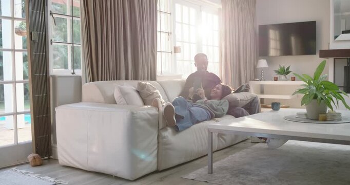 Couple relaxing on white sofa at home, woman raising smartphone, man leaning and viewing content