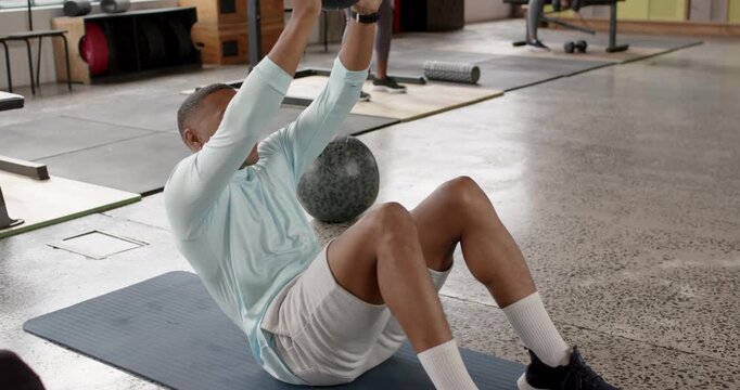 African American gym duo, man holding med ball overhead on mat performing sit-ups for core strength