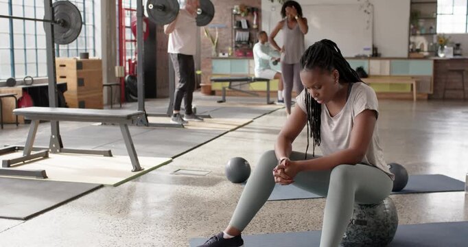 Diverse gym group woman resting between sets on stability ball while man lifting barbell squatting