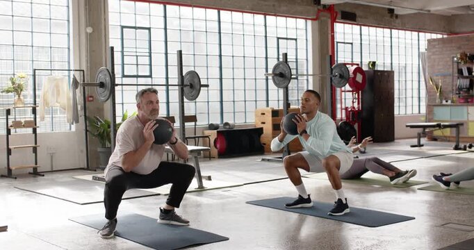 Two men performing synchronized medicine-ball squats on instructor cue in studio, building strength