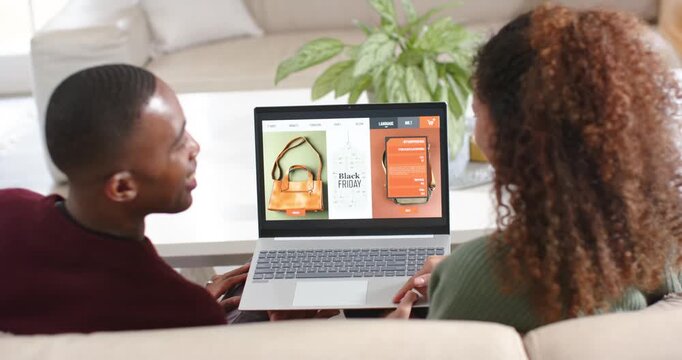 African American couple on sofa browsing Black Friday laptop, comparing handbag vs phone to decide