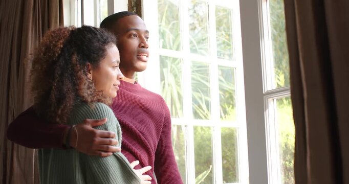 Couple standing by multi-pane window, man holding woman in sweater, sharing moment looking outward
