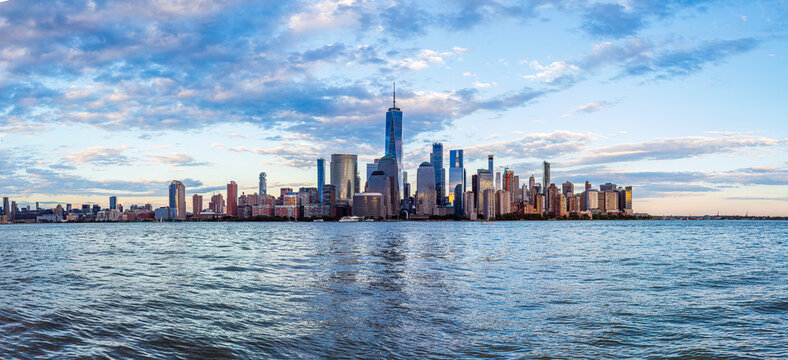 Wide-angle panoramic view of the iconic New York City skyline in the early evening, as shot across the Hudson River from the waterfront in Jersey City, New Jersey.