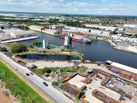 Aerial view of the industrial port area in Goole, featuring a cargo ship docked at the quay, warehouses, storage yards, and a nearby road in Goole, England, United Kingdom.