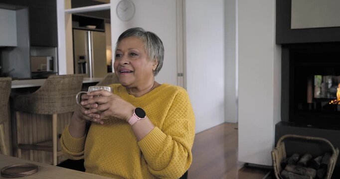 African American senior at table in mustard knit smelling steam lifting glass mug and savoring heat
