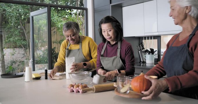 Diverse female friends reaching for flour, pouring into bowl at kitchen island making batter