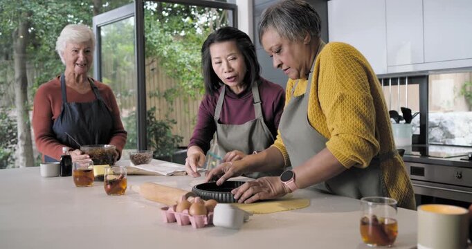 Three female cooks in aprons rolling dough consulting recipe making tart crust kitchen