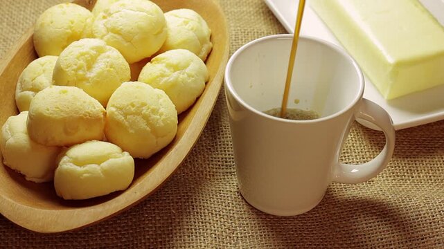 Authentic Brazilian cheese bread served with butter on a rustic burlap cloth, while fresh coffee is served in a white ceramic cup