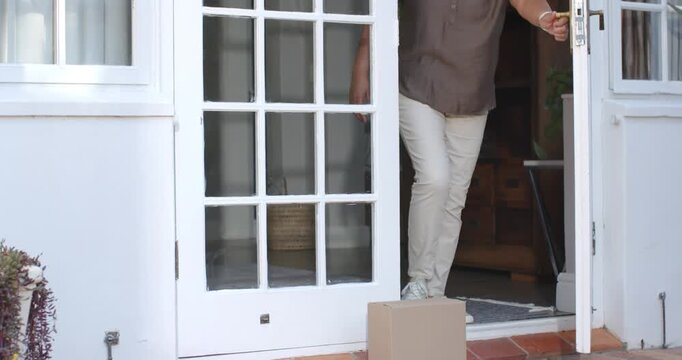 African American Senior woman seeing box at porch opening door bending  and  lifting, retrieving par